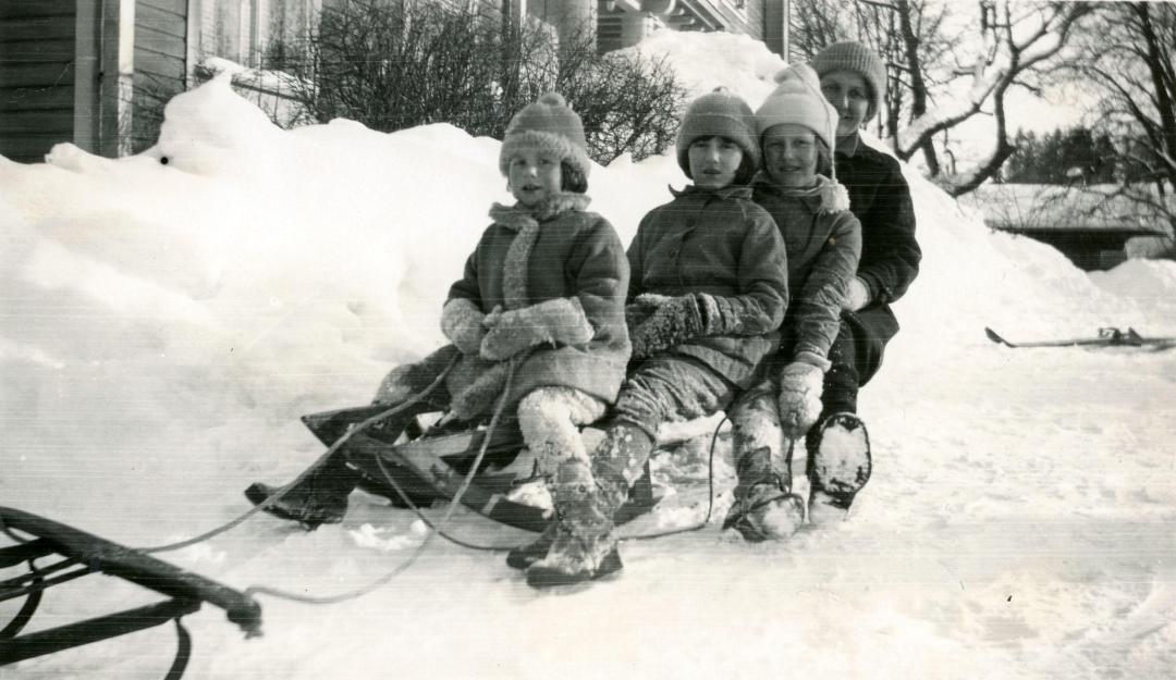 Kolme lasta ja nainen istuvat vanhanaikaisen kelkan kyydissä 1930-luvulla.